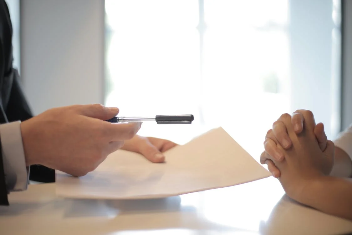 A person handing over a pen and paper to another person
